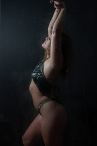 woman in black lingerie is standing in the shower with both arms raised as khim higgins boudoir takes her photos