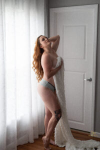 A woman holding a blanket is posing for her boudoir session in Orlando.